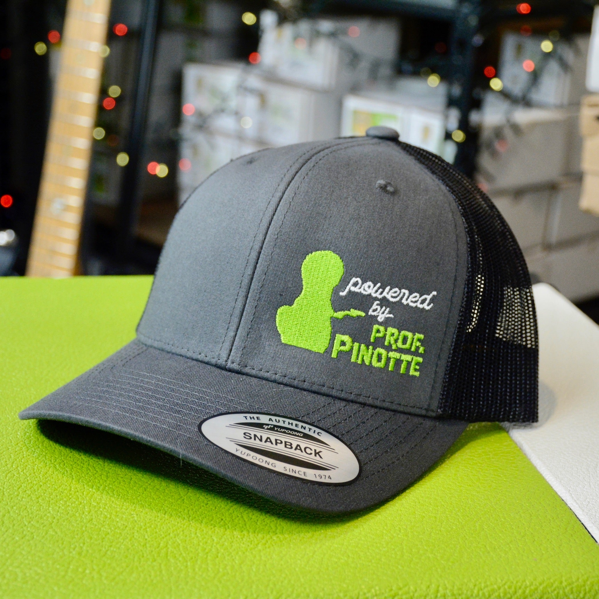 GUPTech Powered by Prof. Pinotte embroided trucker cap, charcoal grey and lime green on a Yupoong snapback cap.